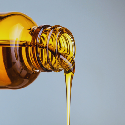 Amber glass bottle with Argan oil being poured against a light blue background