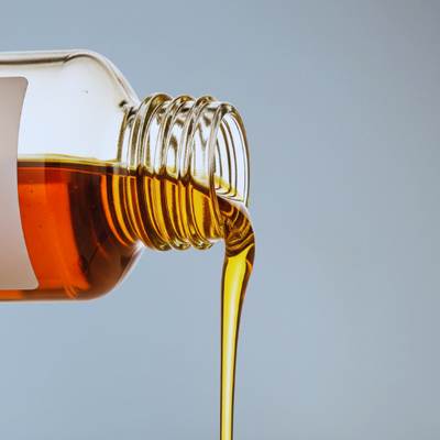 Bottle of Jojoba Oil flowing out against a light Blue background