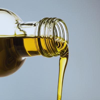 Bottle of olive oil being poured against a gray background